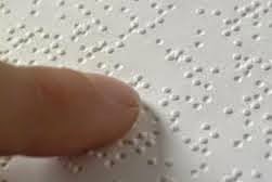 La imagen muestra un dedo en un papel caña escrito en braille